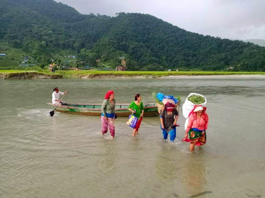 घाँसको भारी लिएर डुङ्गाबाट घर फर्कंदै स्थानीय महिला